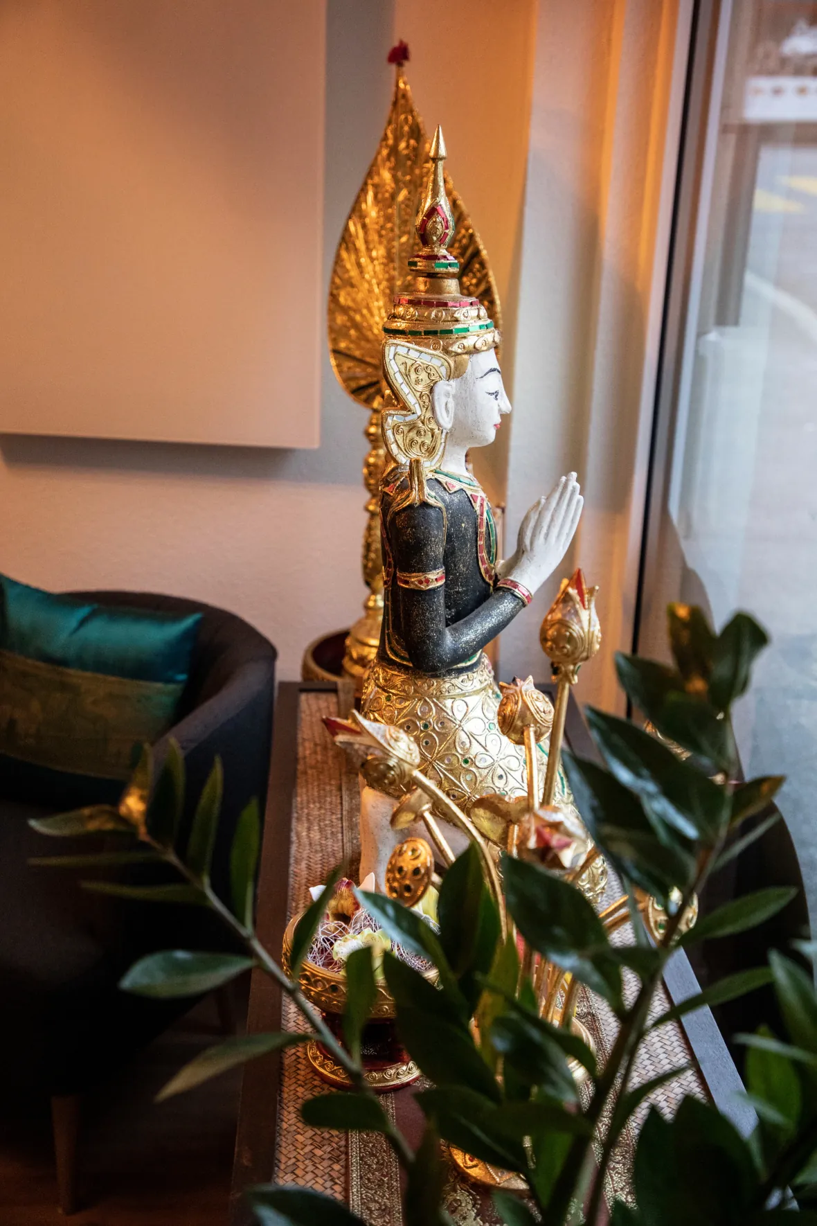 Thailändische Figur mit Grünpflanzen am Fenster